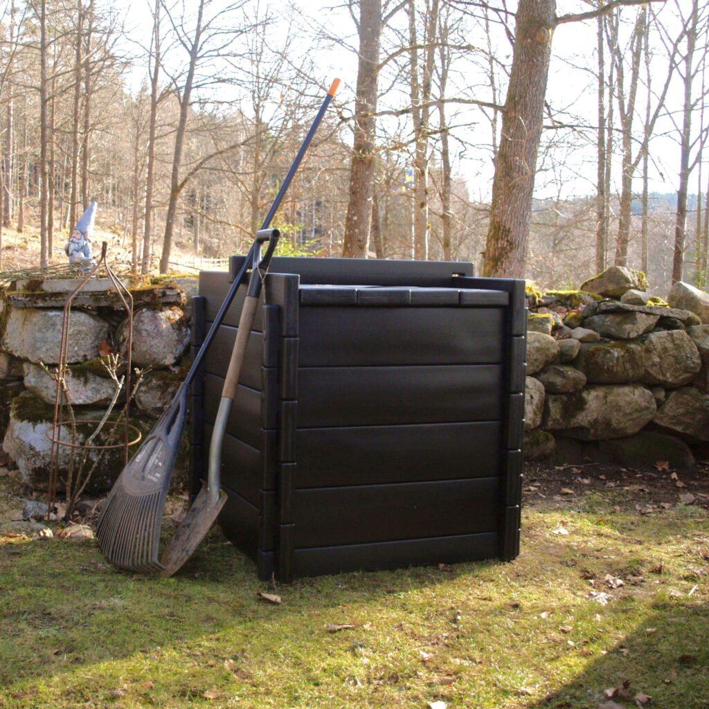 En Biokub 420 liter vid en stenmur i en solig trädgård